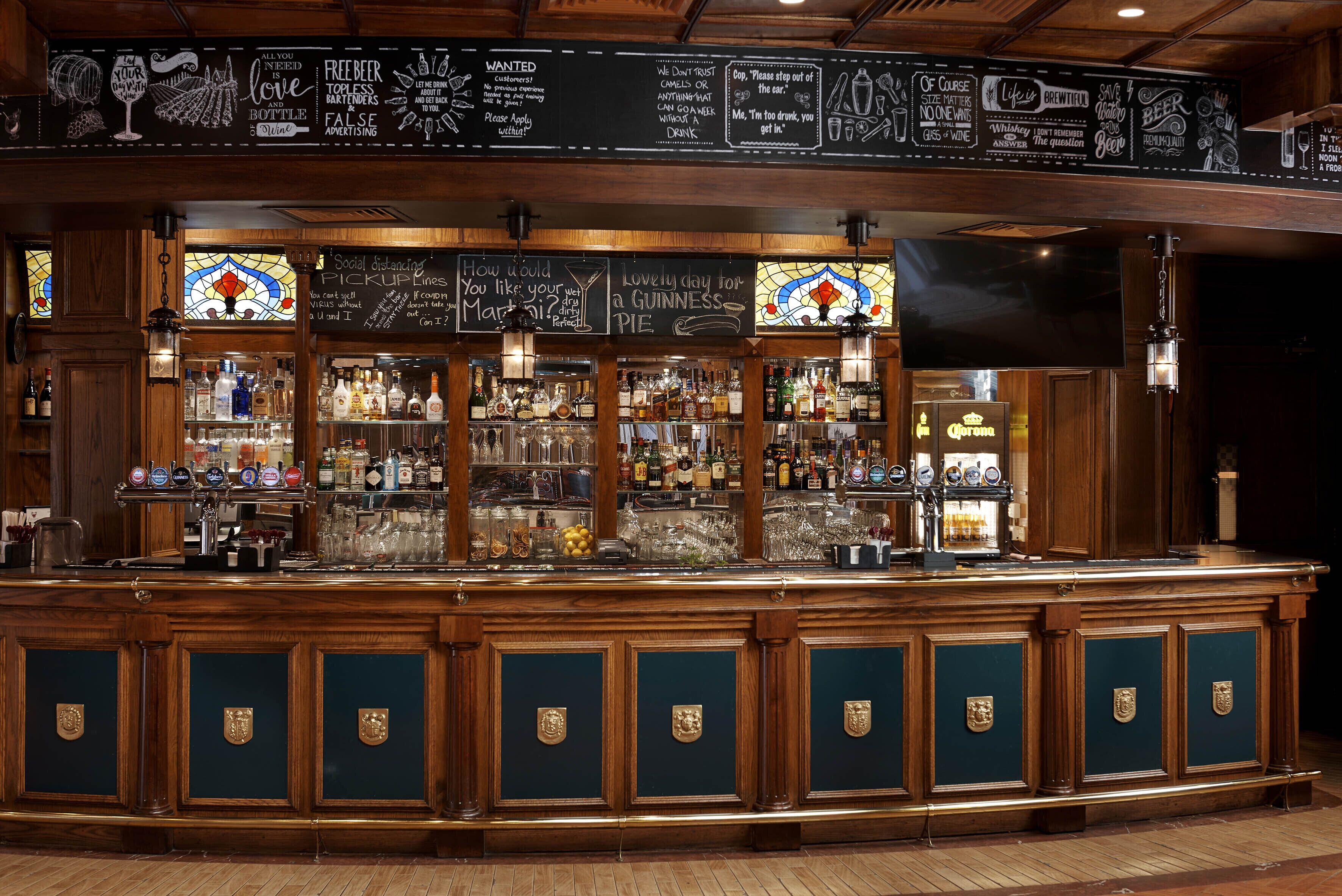 A bar with wooden cabinets, a selection of bottles, glasses, and a chalkboard menu.