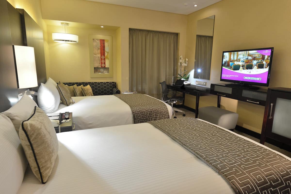 A hotel room with two beds, a desk with a computer, a TV, and a large window with curtains.
