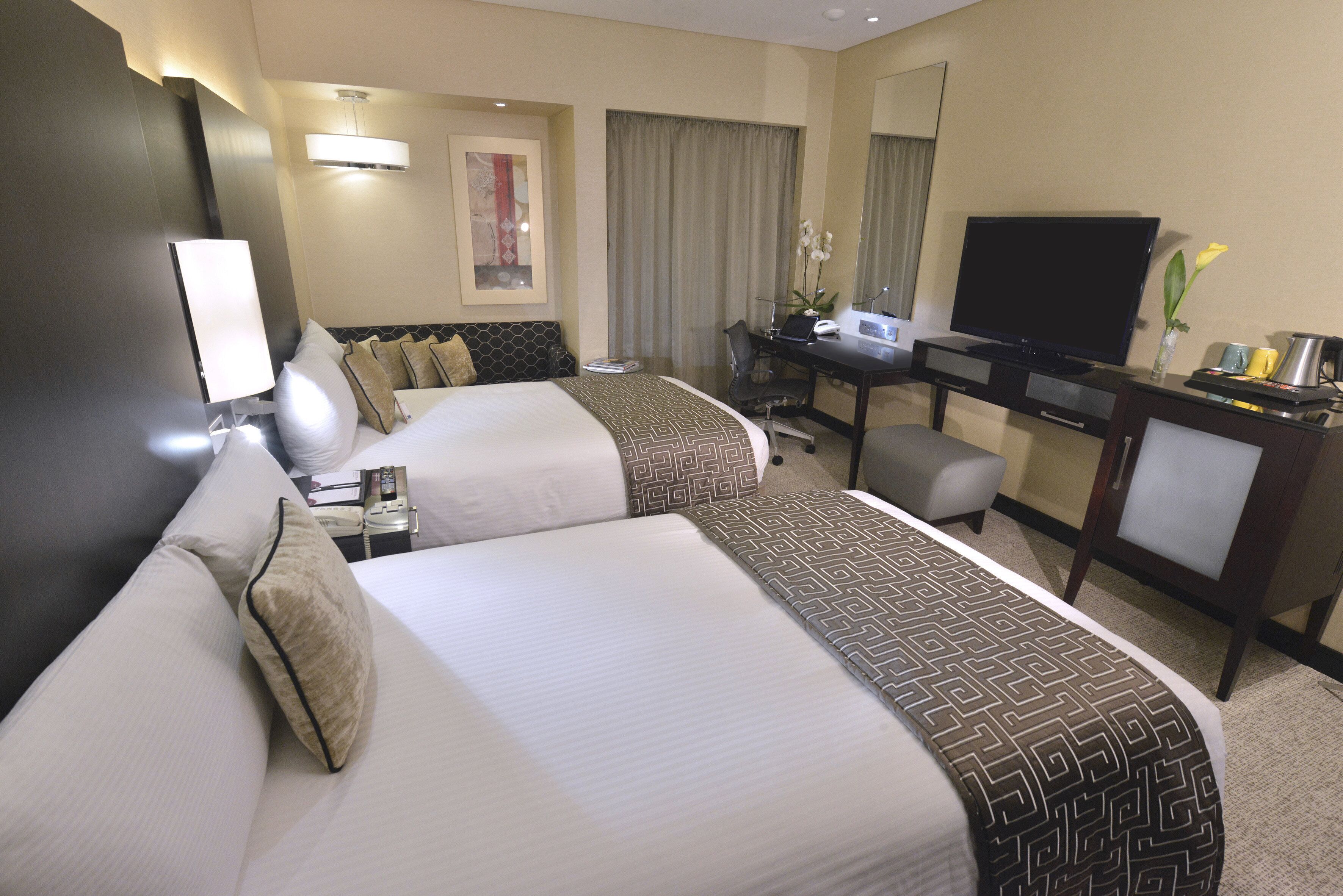 A hotel room with two beds, a desk, a television, and a mirror.