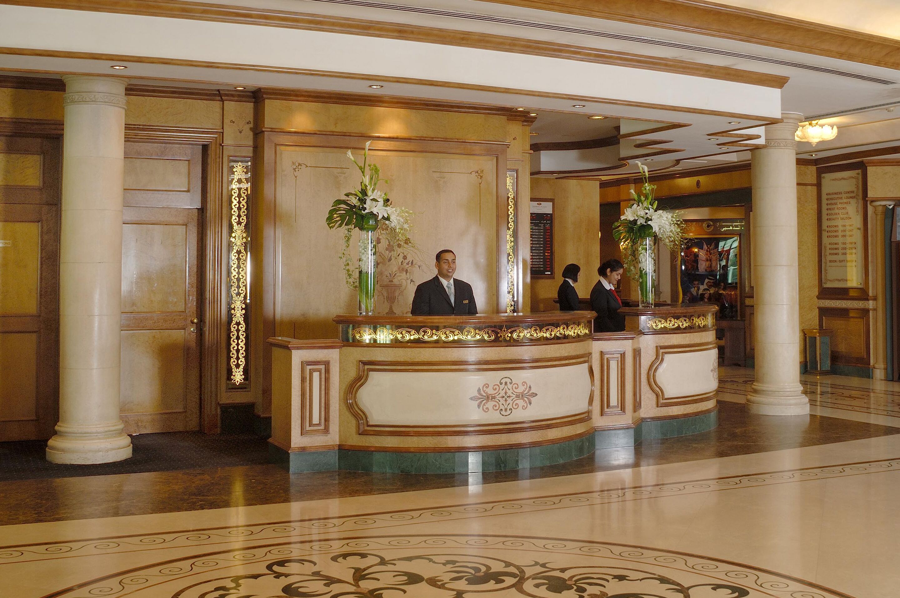 A reception area with a marble floor, a reception desk, and two large vases with flowers.