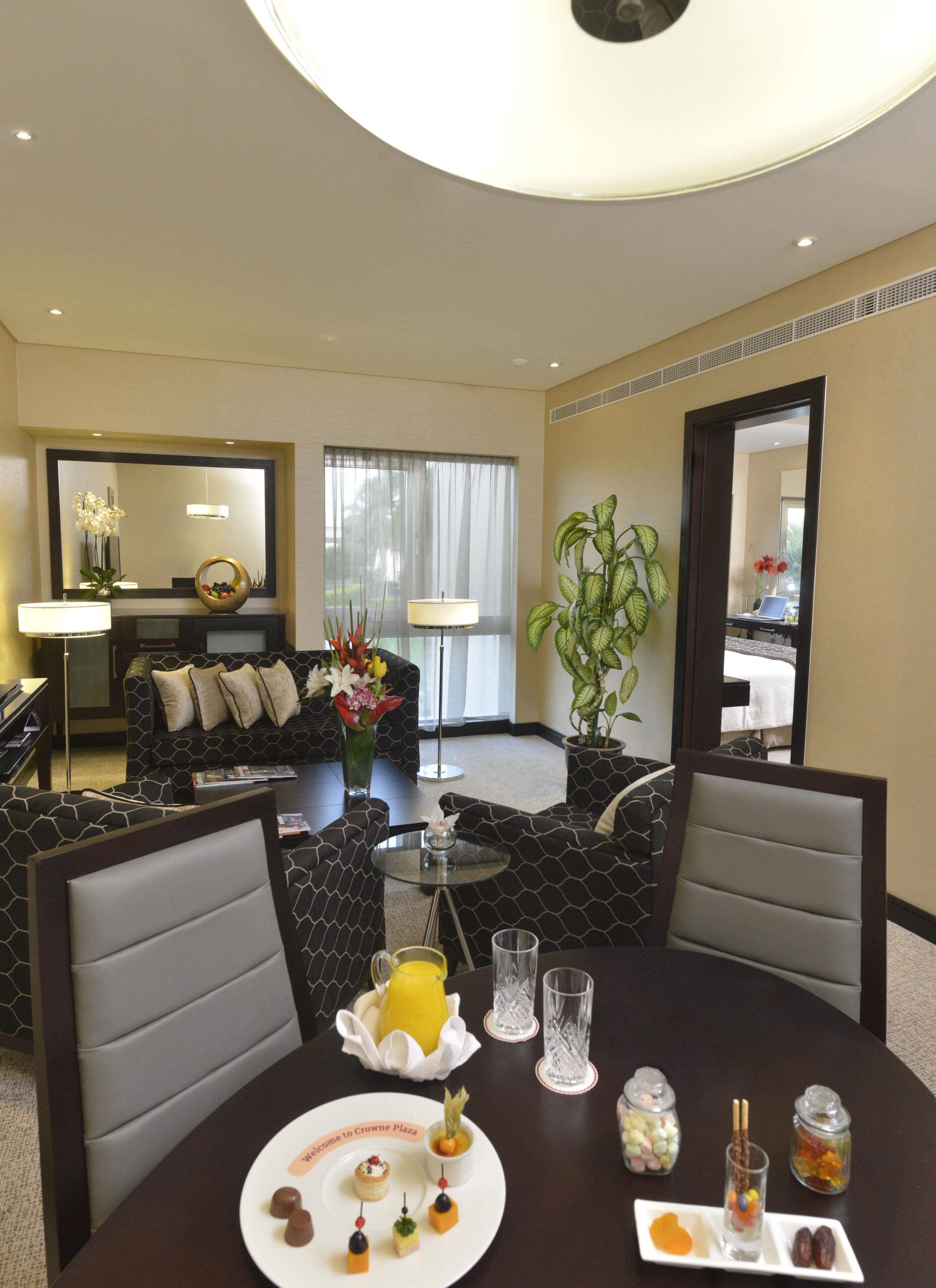 A hotel room with a dining area, a sofa, a coffee table, and a dining table set with food and drinks.