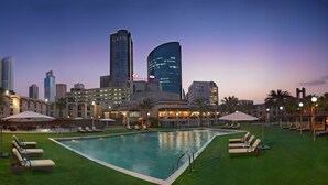 A hotel pool area with lounge chairs and umbrellas, surrounded by high-rise buildings.
