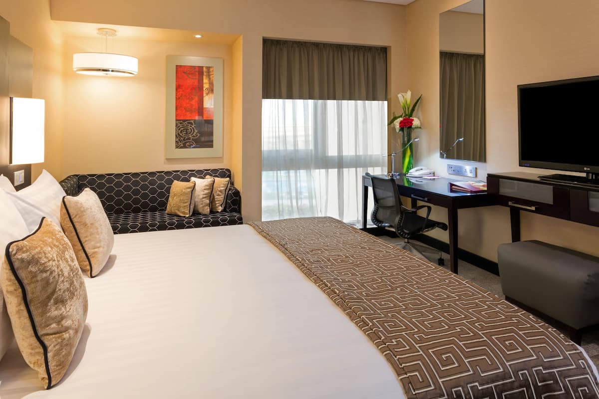 A hotel room with a large bed, a desk with a chair, a television, and a window with curtains.