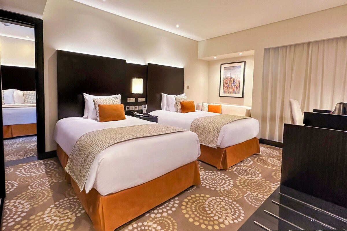 Una habitación de hotel con dos camas, un escritorio y un ventanal con cortinas.
