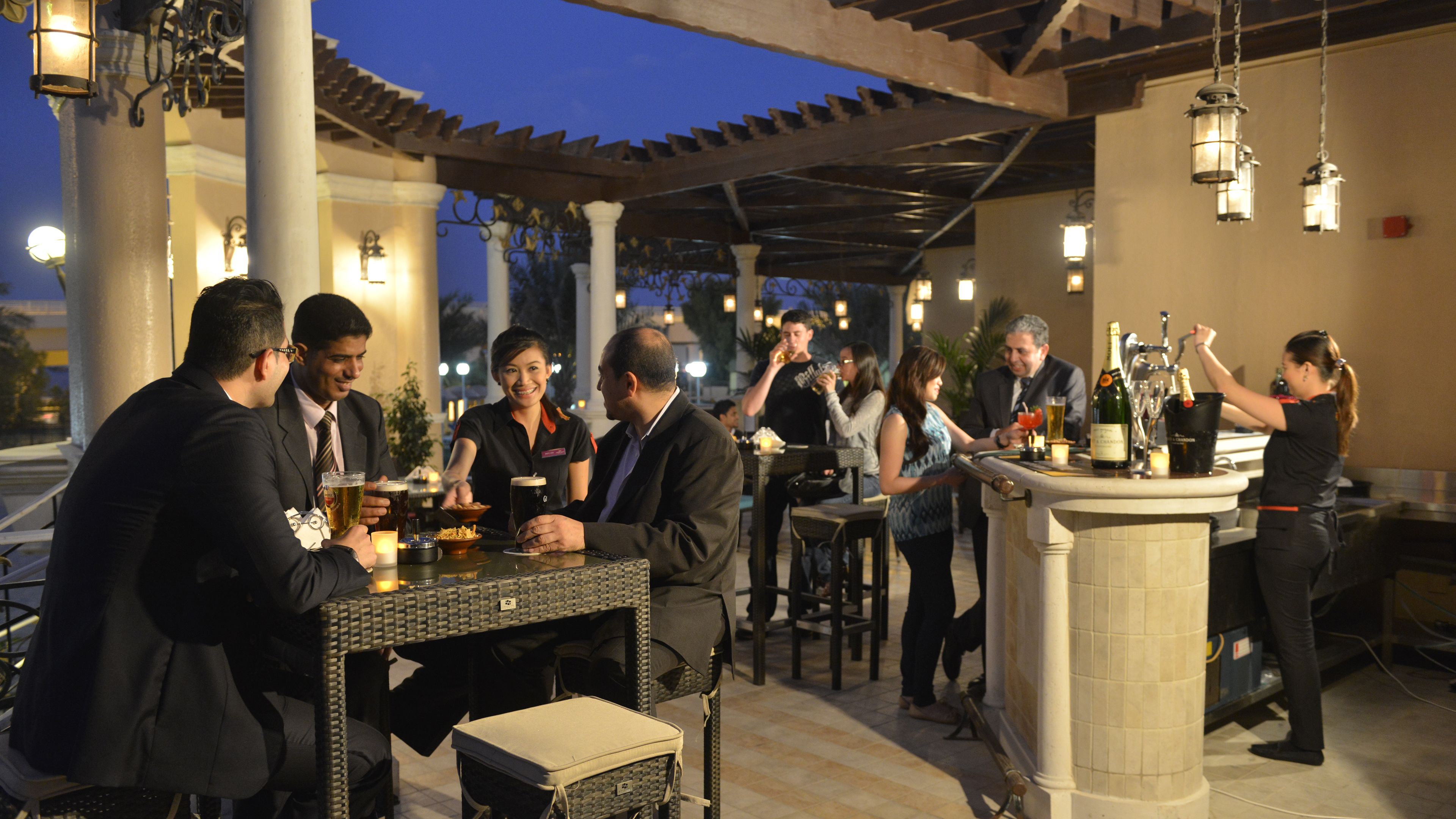 An outdoor bar area with tables and chairs, a bartender, and guests enjoying drinks.
