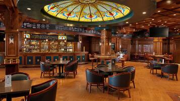 A bar area with wooden furniture, a stained glass ceiling, and a bar counter with various bottles.