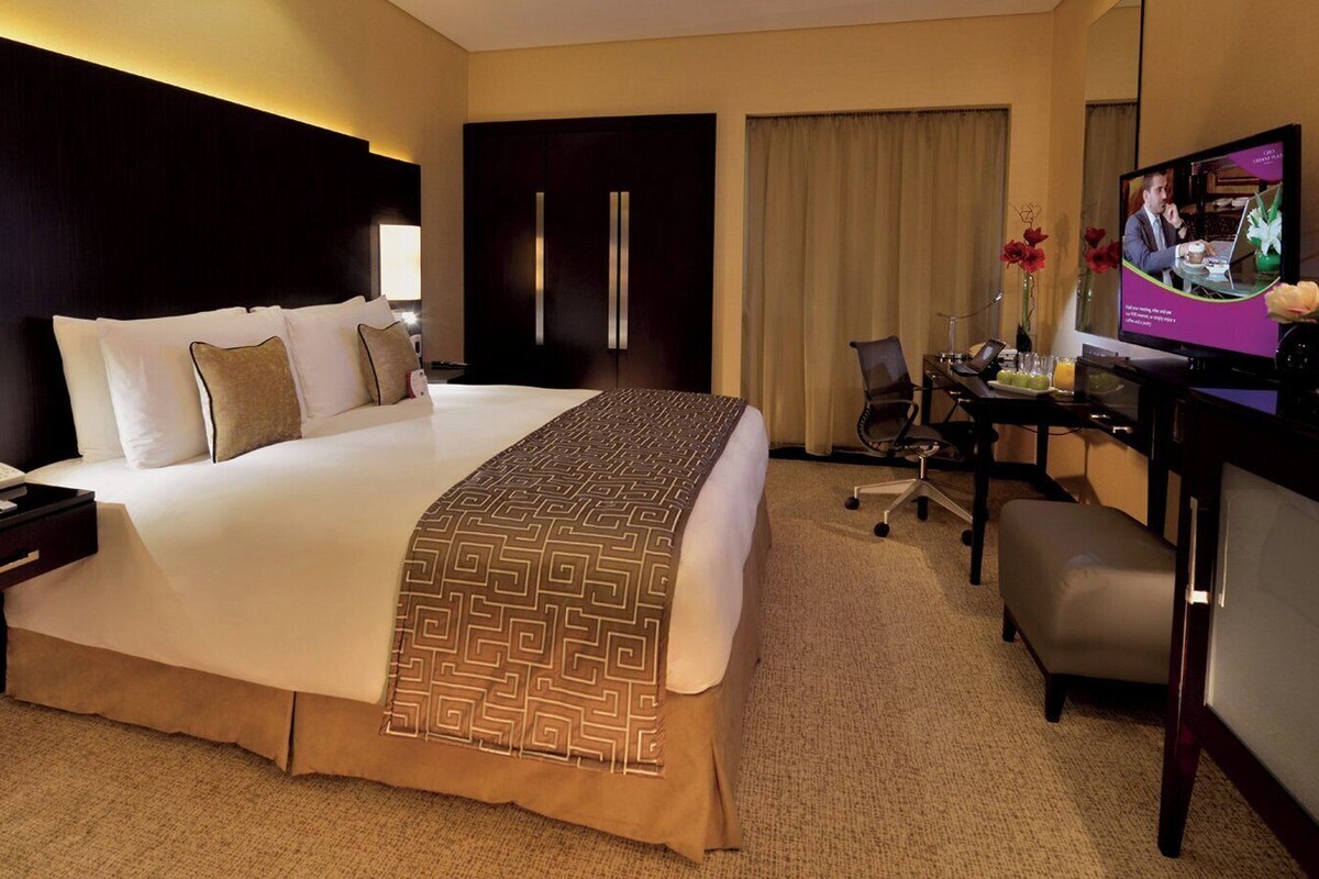 Una habitación de hotel con una cama grande, un escritorio con computadora, televisión y un mini bar.