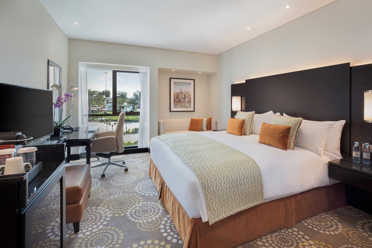A modern hotel room with a large bed, a desk with a computer, a chair, and a television.