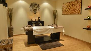 Relax in a serene spa room with a massage table, dark wooden bench, and a vase of dried reeds.