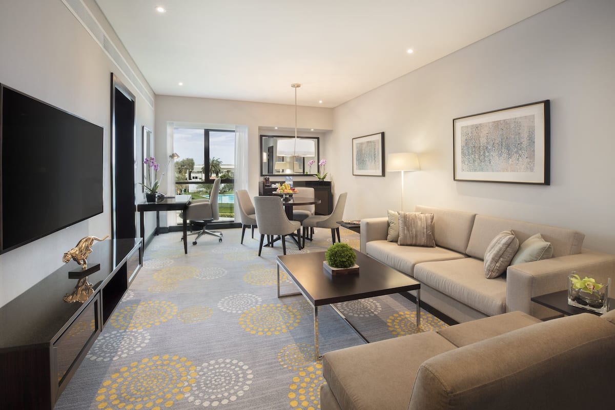 A modern living room with a flat-screen TV, a sofa, a coffee table, and a dining area with chairs and a desk.