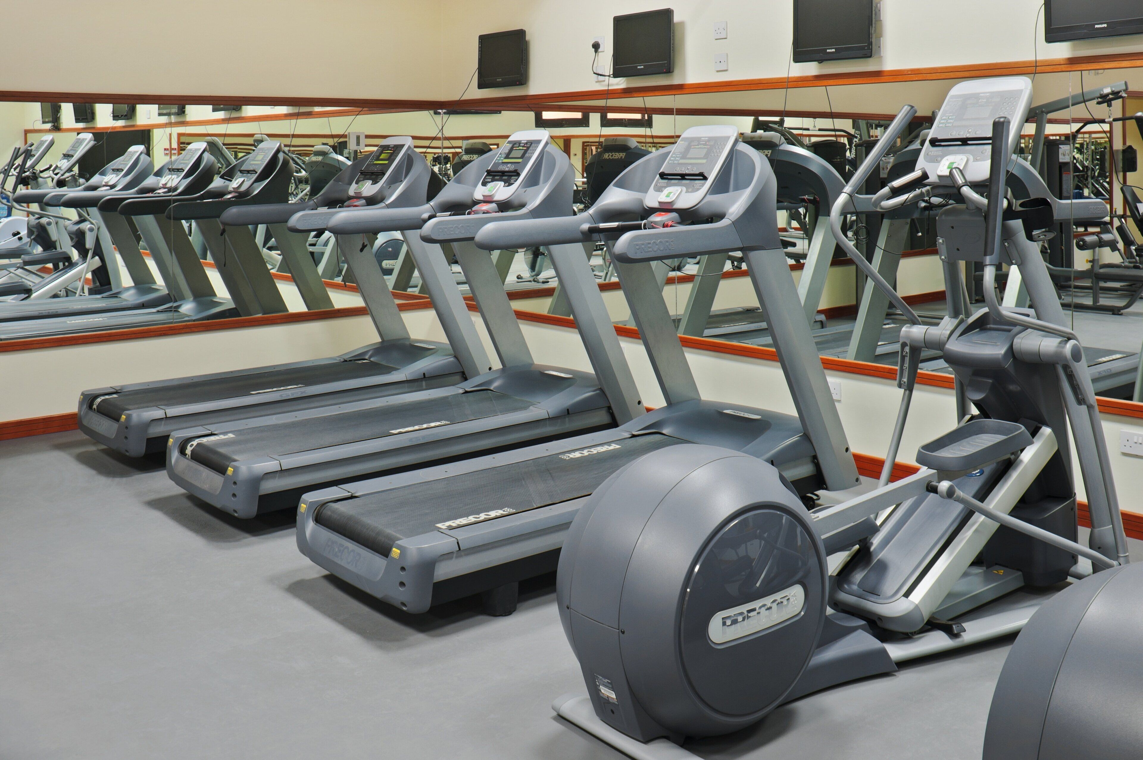 A row of treadmills in a gym with mirrors on the wall.