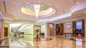 Eine geräumige Lobby mit einer imposanten Treppe, einem Chandelier und einer Rezeption.