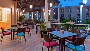 Ein Außenbereich mit Terrasse, Tischen, Stühlen, einer Fontäne und Blick auf das Gebäude im Hintergrund.