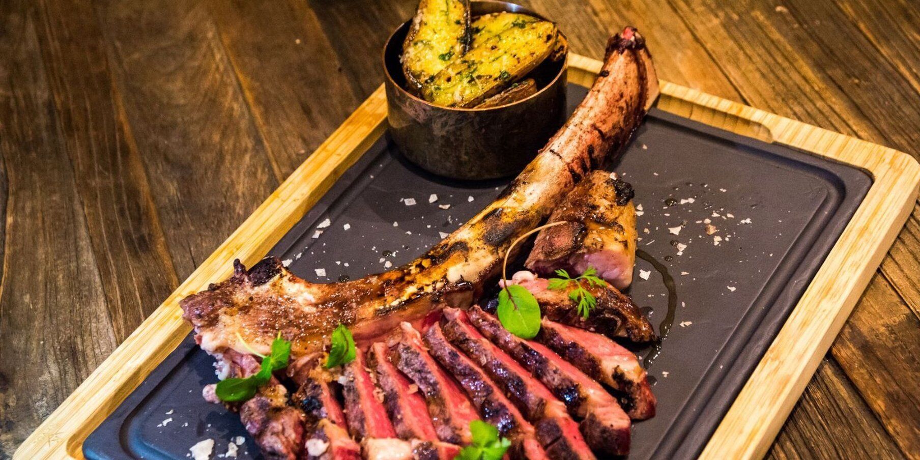 Un bistec con una guarnición de papas asadas en un plato negro.