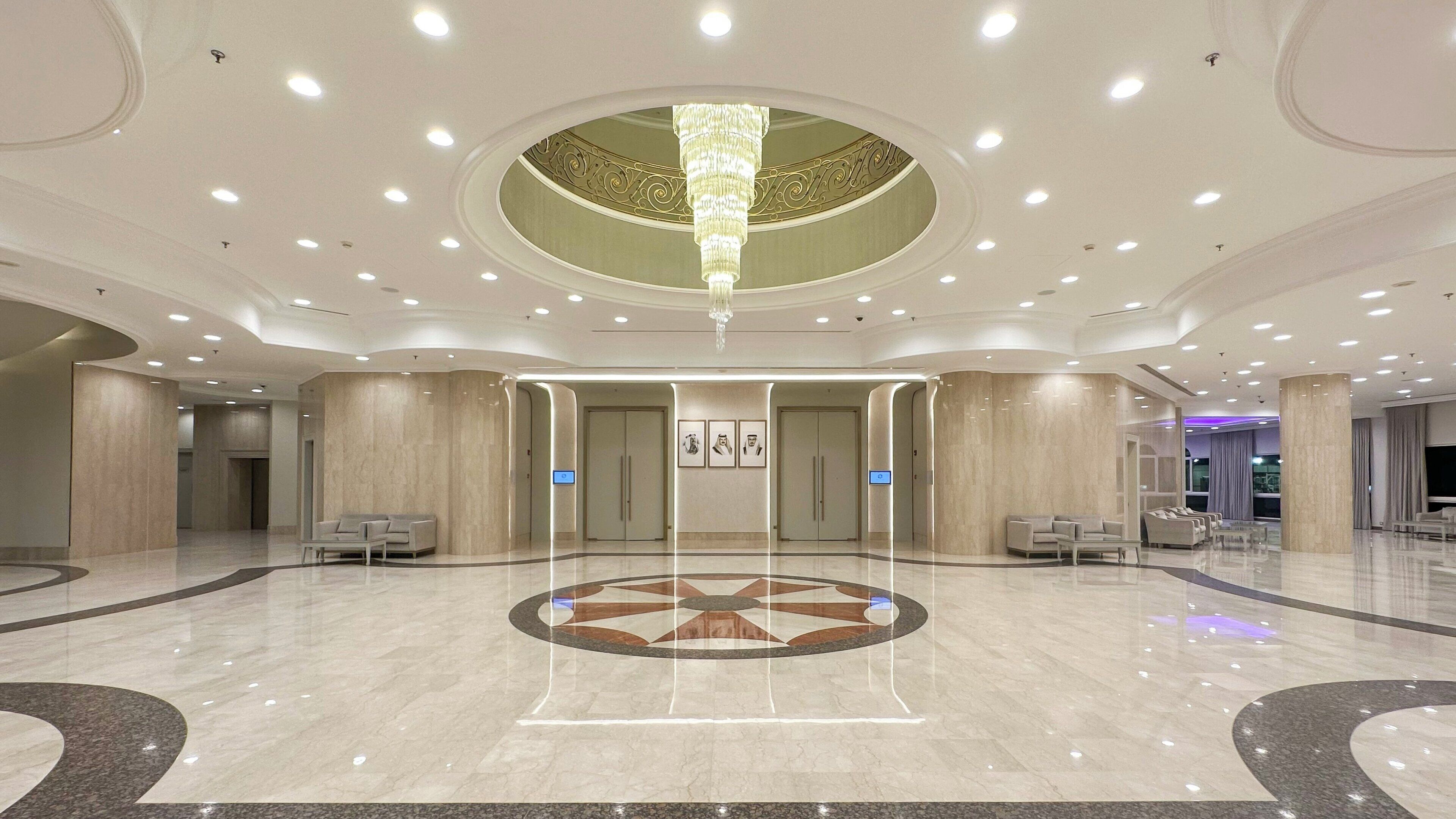 A spacious lobby with a central chandelier, marble flooring, and seating areas.