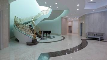 Una gran escalera con barandales ornamentados, un piano y una zona de estar en un vestíbulo amplio con un diseño de piso curvo.