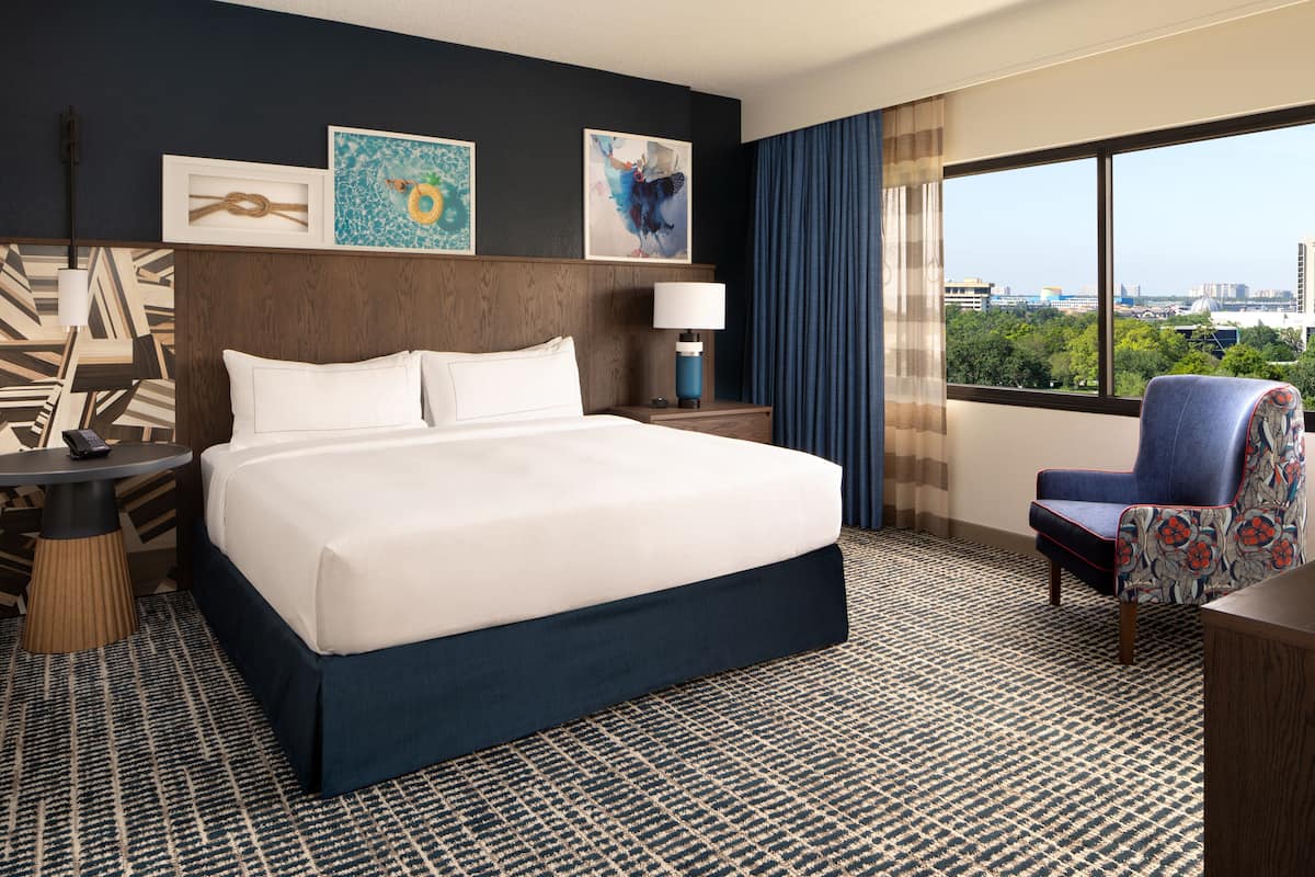 Ein Hotelzimmer mit einem großen Bett, einem Schreibtisch, einem Stuhl und Blick auf die Stadt.