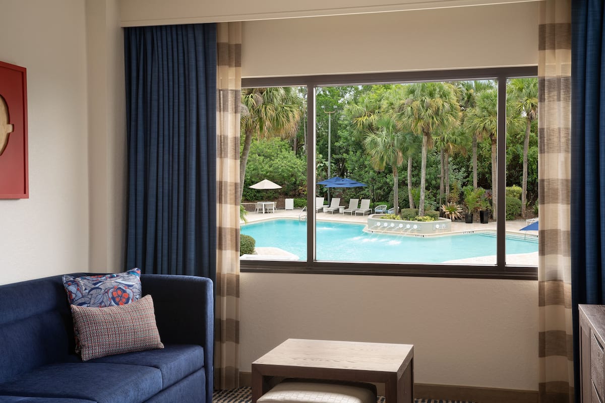 Ein Zimmer mit Blick auf einen Swimmingpool, einem blauen Sofa, einem kleinen Tisch und einem Fenster mit Vorhängen.