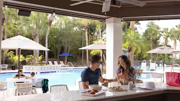 A poolside bar area with a pool view, outdoor seating, and umbrellas.