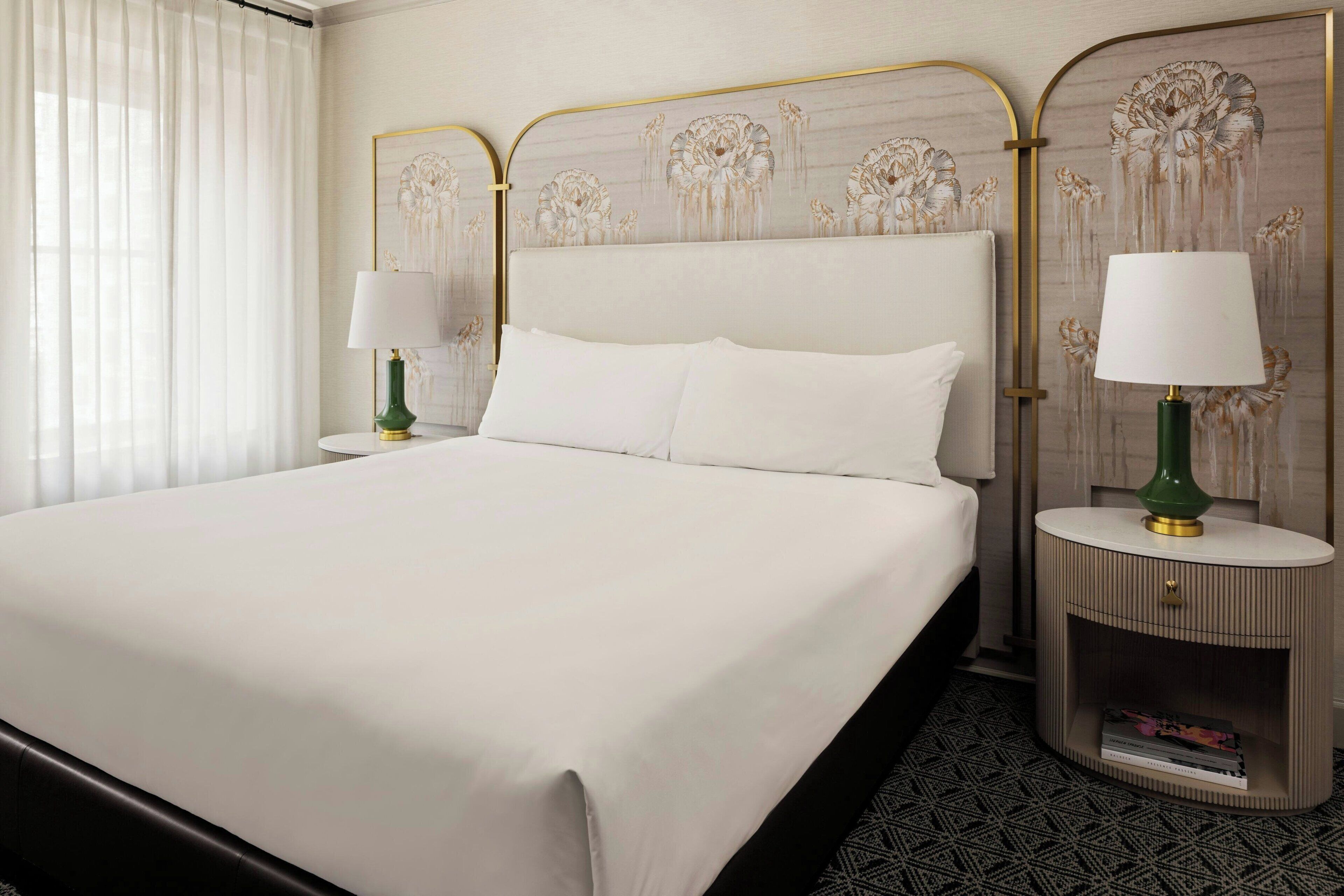 A hotel room with a large bed, two bedside tables with lamps, a decorative headboard, and a patterned rug.