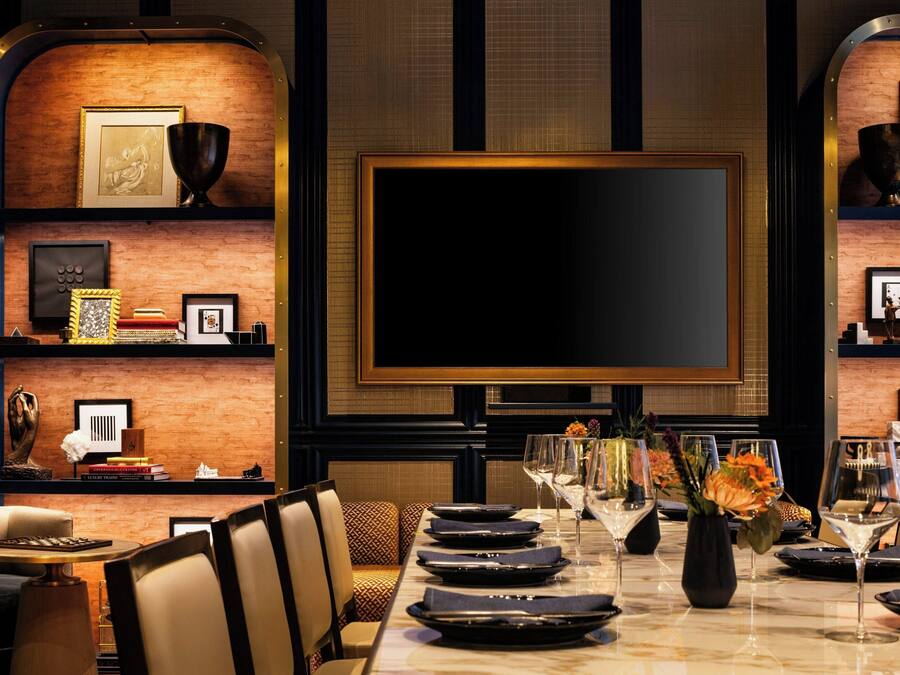 A dining area with a long table set for a meal, flanked by chairs, and a large flat-screen TV mounted on the wall.