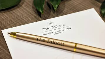 Una tarjeta blanca con la inscripción 'The Talbott Autograph Collection Hotels', colocada sobre una superficie texturizada y una pluma dorada sobre ella.