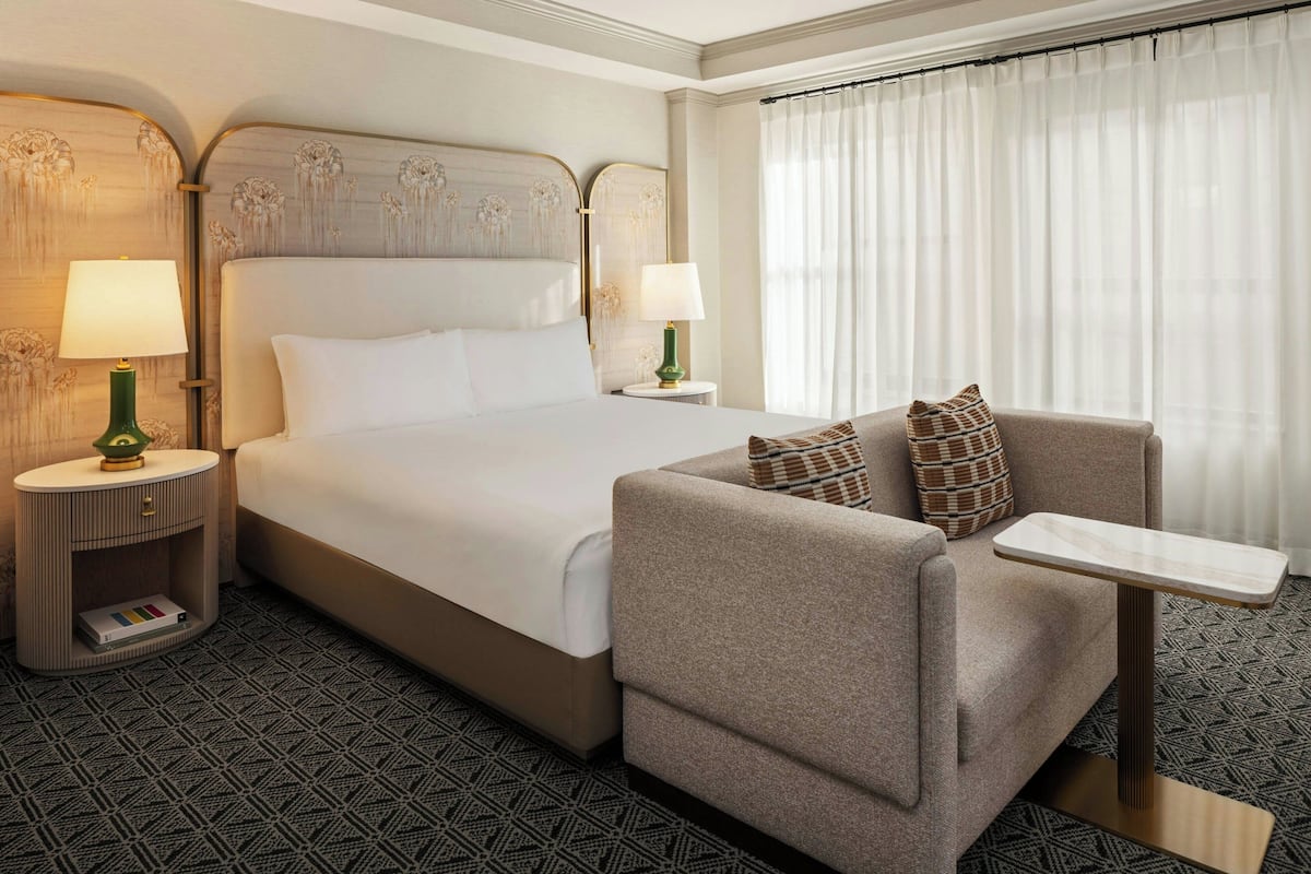 A hotel room with a bed, a sofa, a small table, and two bedside tables with lamps.