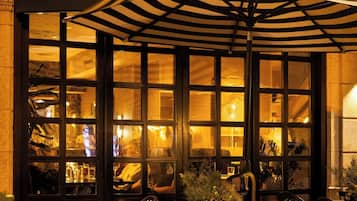 The exterior of a hotel named 'LAUREL' with a large illuminated sign, outdoor seating area with tables and chairs, and a canopy umbrella.