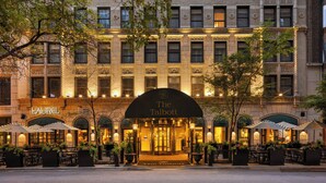 A hotel entrance with a marquee sign, outdoor seating, and a well-lit facade.