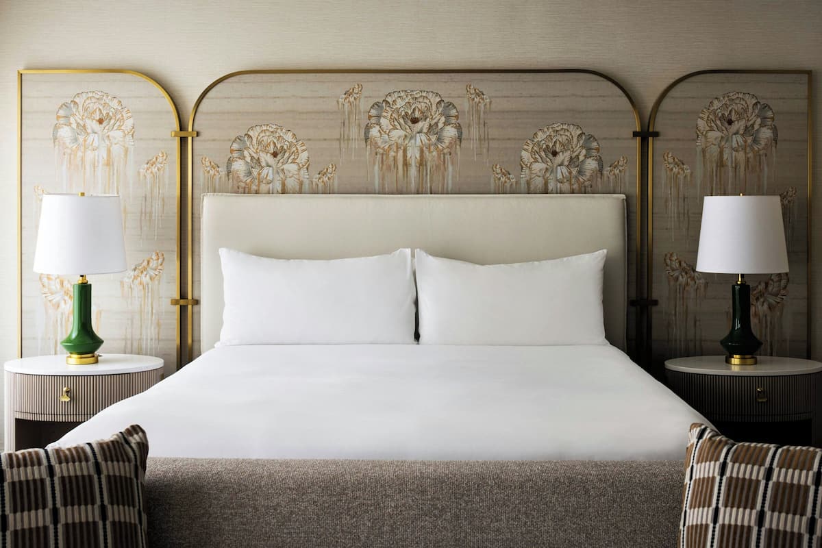 A neatly made bed with white linens and two pillows, flanked by two nightstands with lamps and decorative vases.