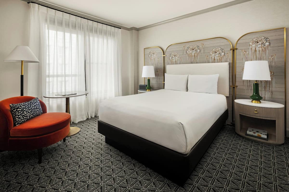 A hotel room with a large bed, two bedside tables with lamps, a red armchair, and a patterned carpet.