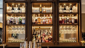 A bar with three wooden shelves filled with bottles and glasses.