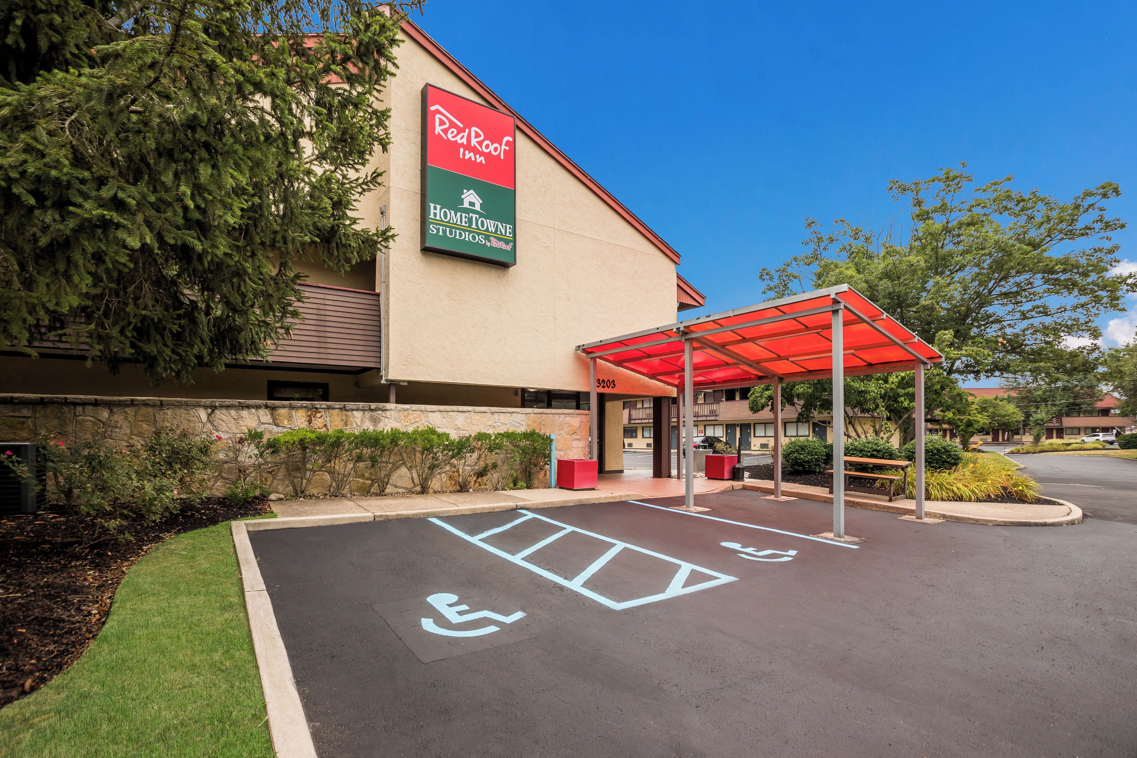 A Red Roof Inn with a covered parking area, handicap accessible parking, and a stone wall with greenery.