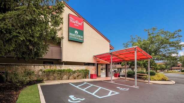 A Red Roof Inn with a covered parking area, handicap accessible parking, and a stone wall with greenery. - Red Roof Inn Princeton - Ewing (Lawrenceville)
