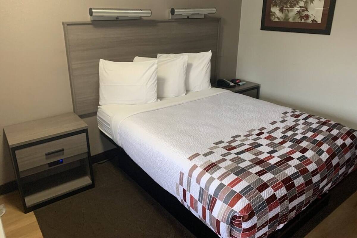 Ein Hotelzimmer mit Bett, Nachttisch, Schublade, einer Ablagefläche und einem Wandbild.