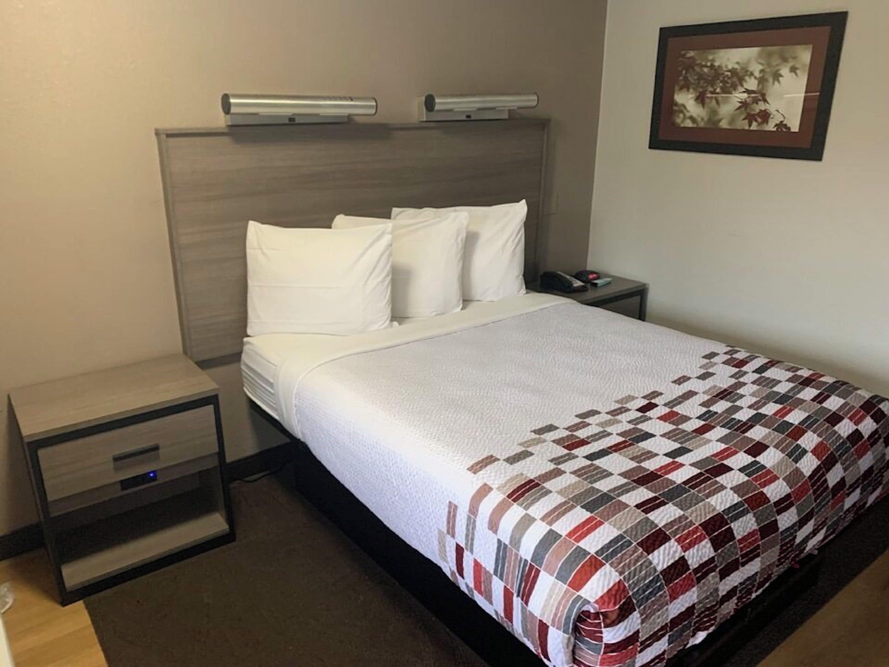 A hotel room with a bed, a bedside table, a nightstand, and a wall-mounted picture.