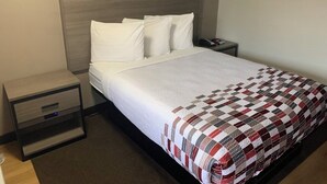 A hotel room with a bed, a bedside table, a nightstand, and a wall-mounted picture. - Red Roof Inn Princeton - Ewing (Lawrenceville)