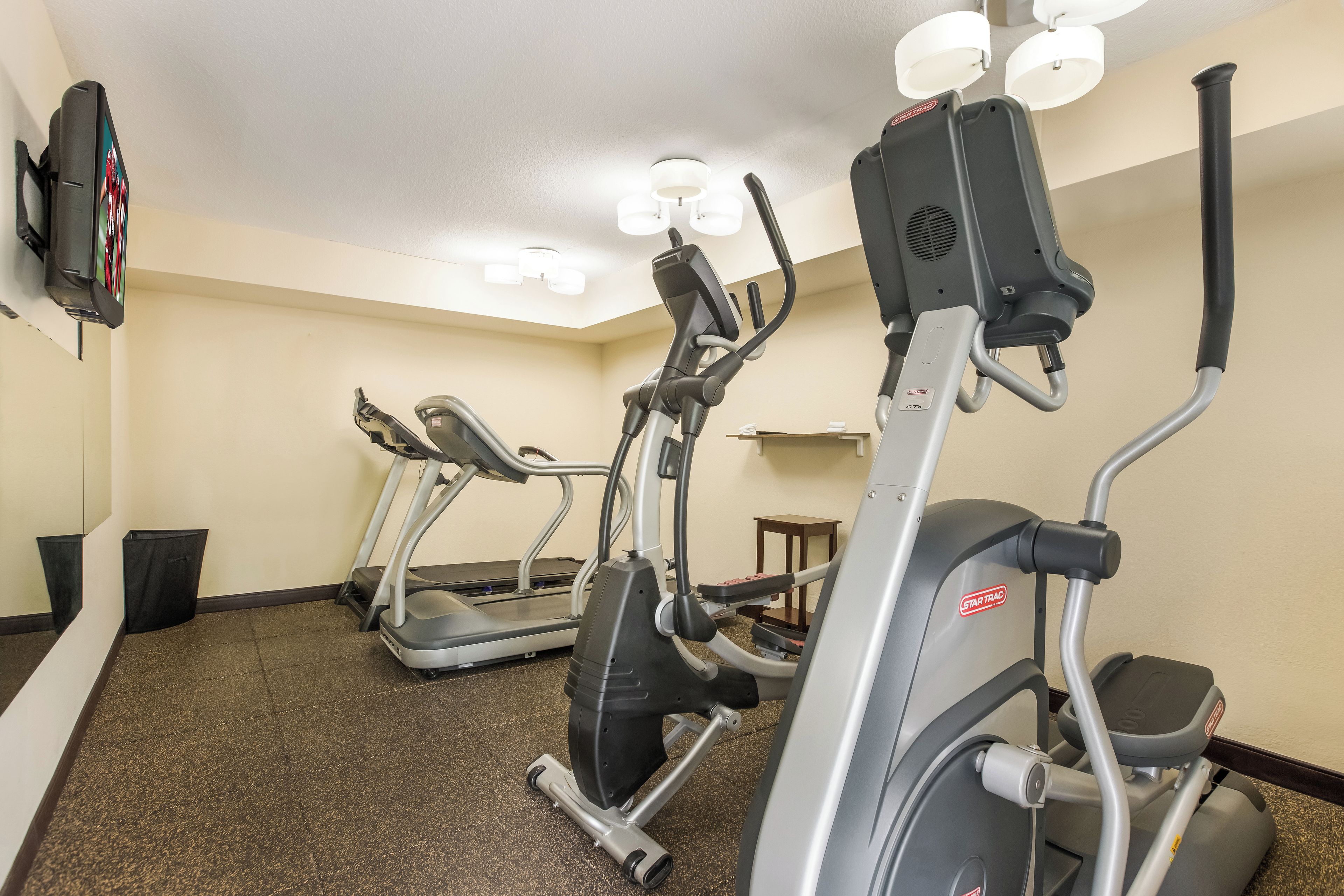 A fitness room with treadmills and elliptical machines, a small table, and a trash bin.
