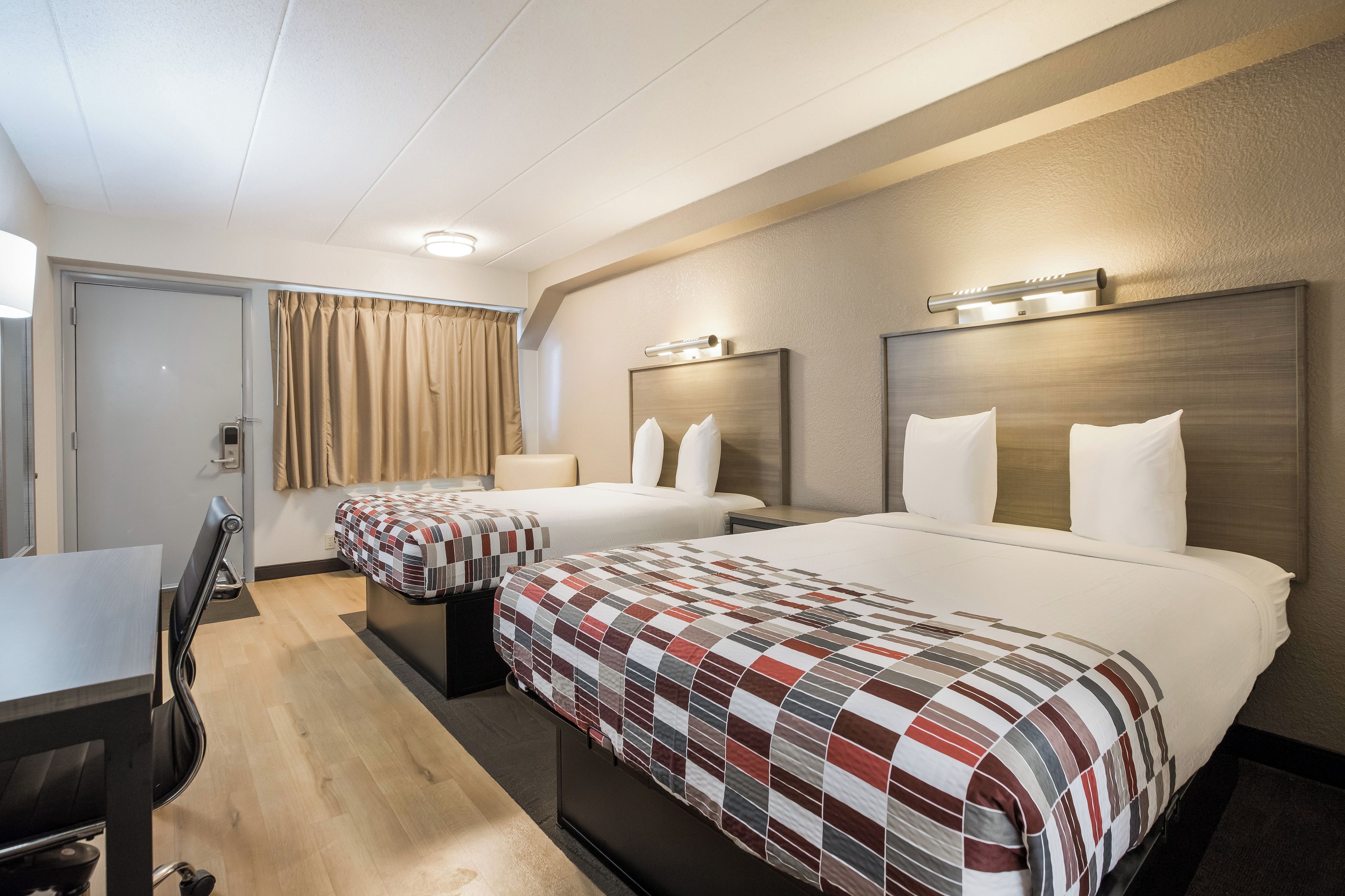 A hotel room with two beds, a desk, and a chair.
