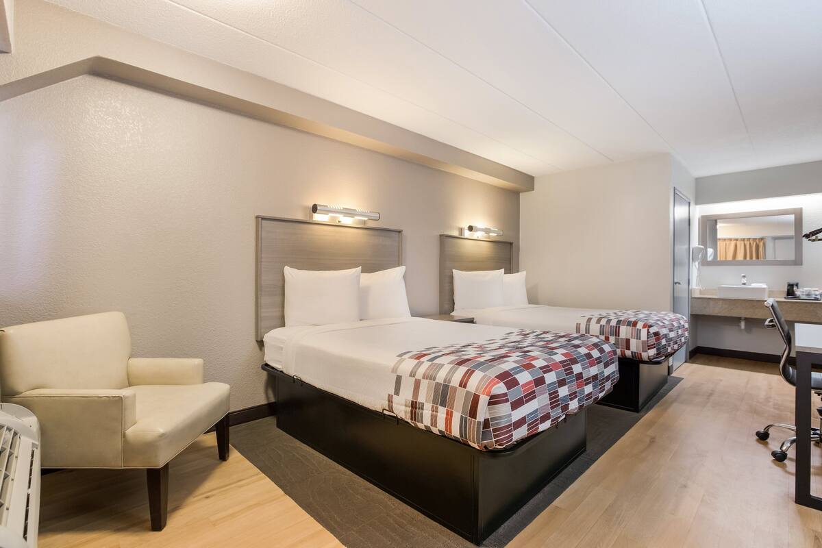 Ein Hotelzimmer mit zwei Betten, einem Sessel, einem Schreibtisch und einem Spiegel.