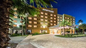 Un hotel Hyatt Place con una entrada bien iluminada, palmeras y un camino de acceso pavimentado.