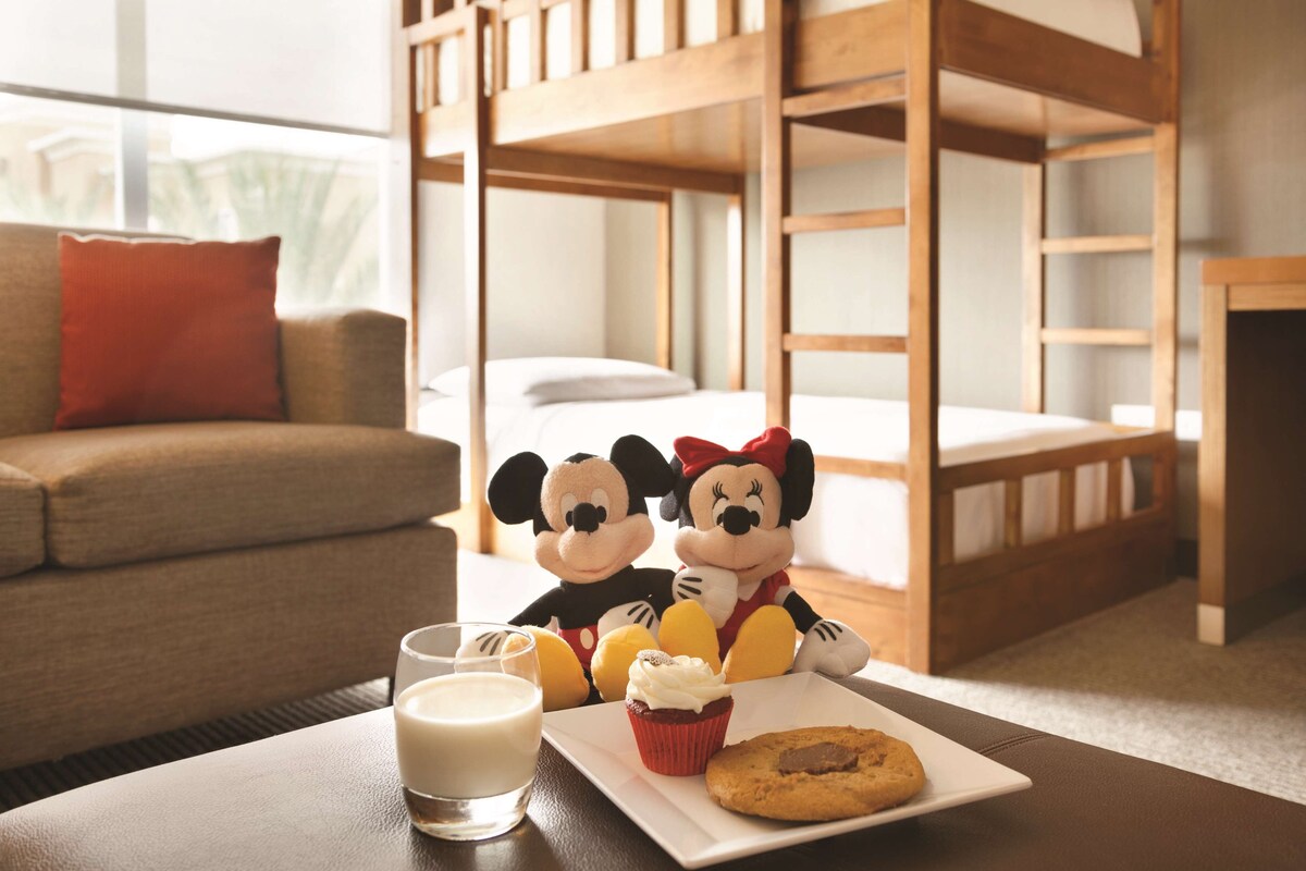 A cozy room with bunk beds, a sofa, and a table with a glass of milk, a cupcake, and a cookie.