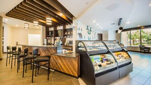 Un café moderno con mostrador de madera, taburetes, una vitrina con pasteles y vistas a palmeras a través de amplias ventanas.