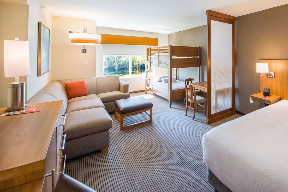 A hotel room with a bunk bed, a sofa, a desk, a chair, and a bedside table.