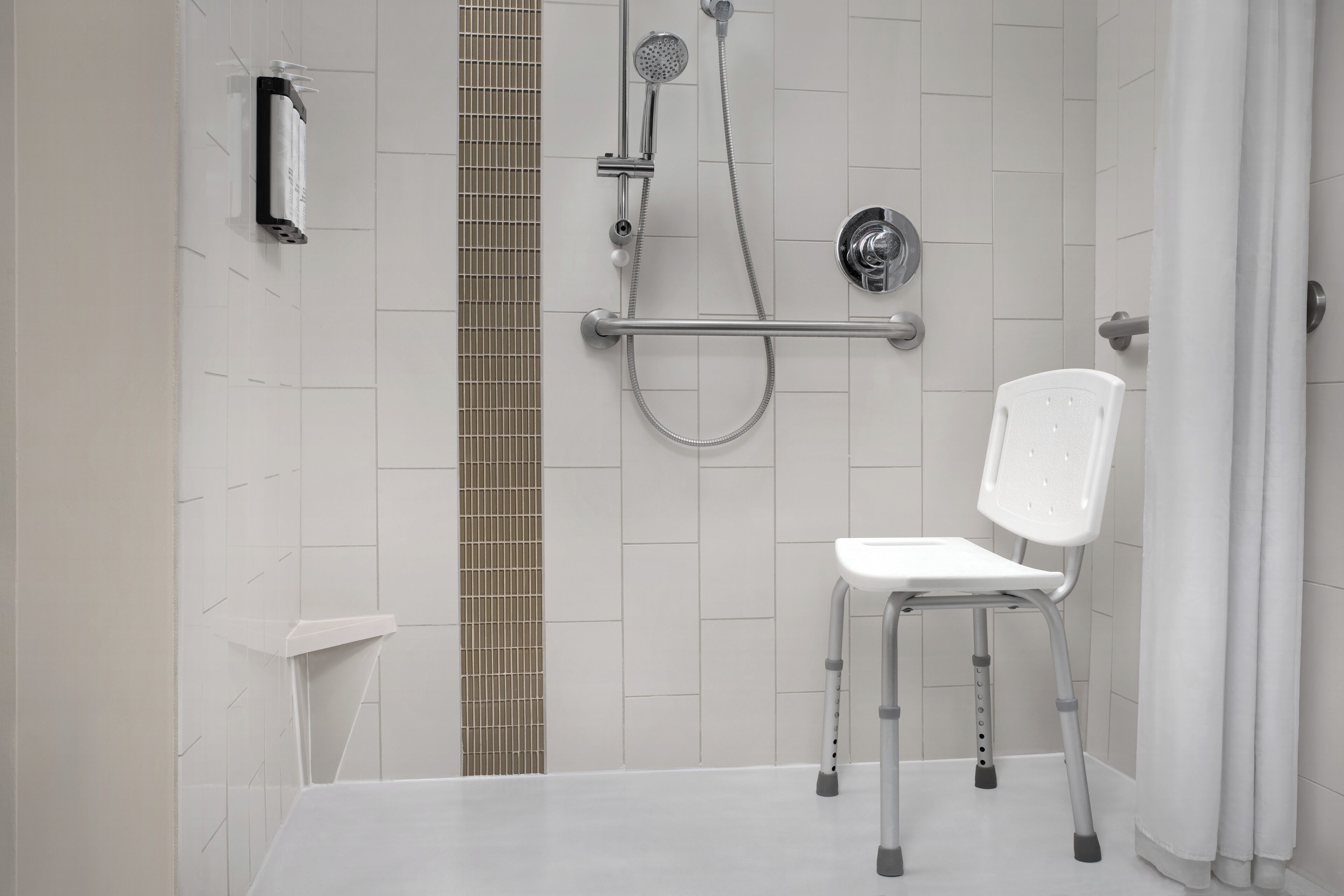 A shower area with a white chair, a handheld showerhead, a wall-mounted showerhead, and a towel rack.