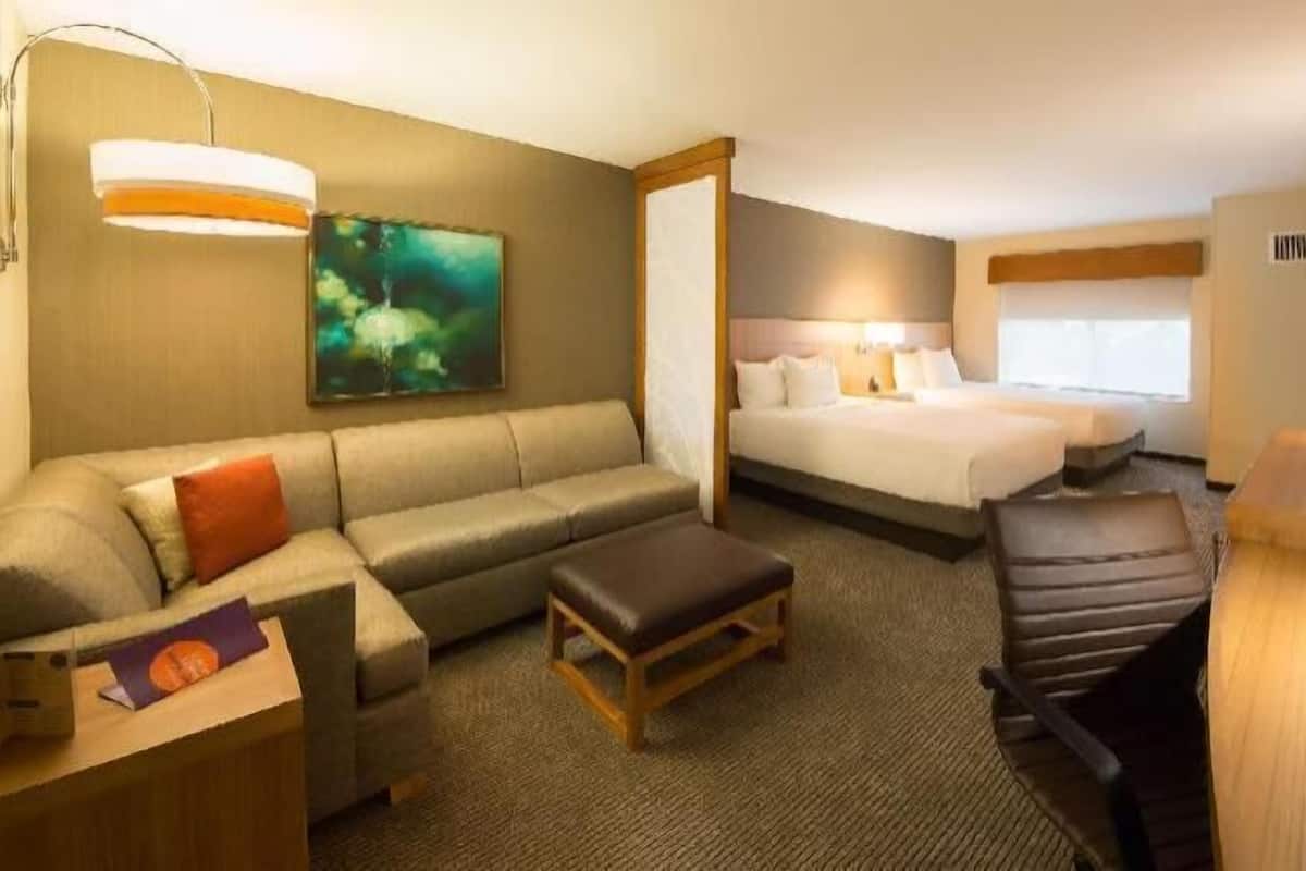 A hotel room with a bed, a sofa, a desk, a chair, a coffee maker, and a painting on the wall.