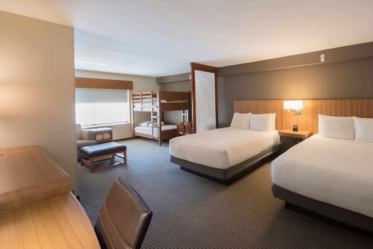 A hotel room with two beds, a desk, a chair, and a small seating area.
