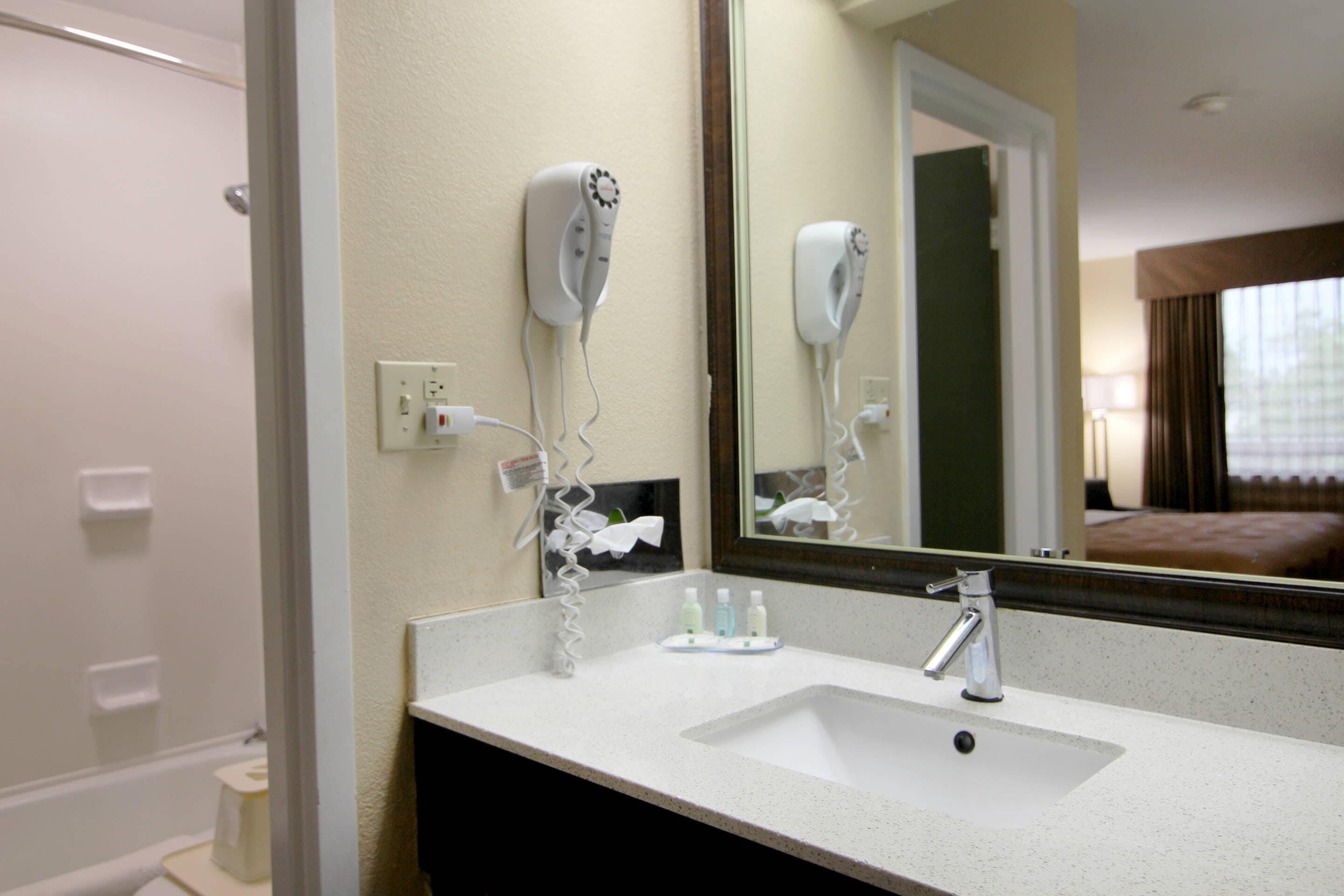 Een hotelbadkamer met een wastafel, spiegel, haardroger en toiletartikelen.