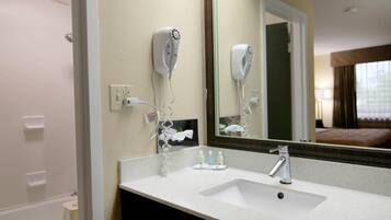 Een hotelbadkamer met een wastafel, spiegel, haardroger en toiletartikelen.