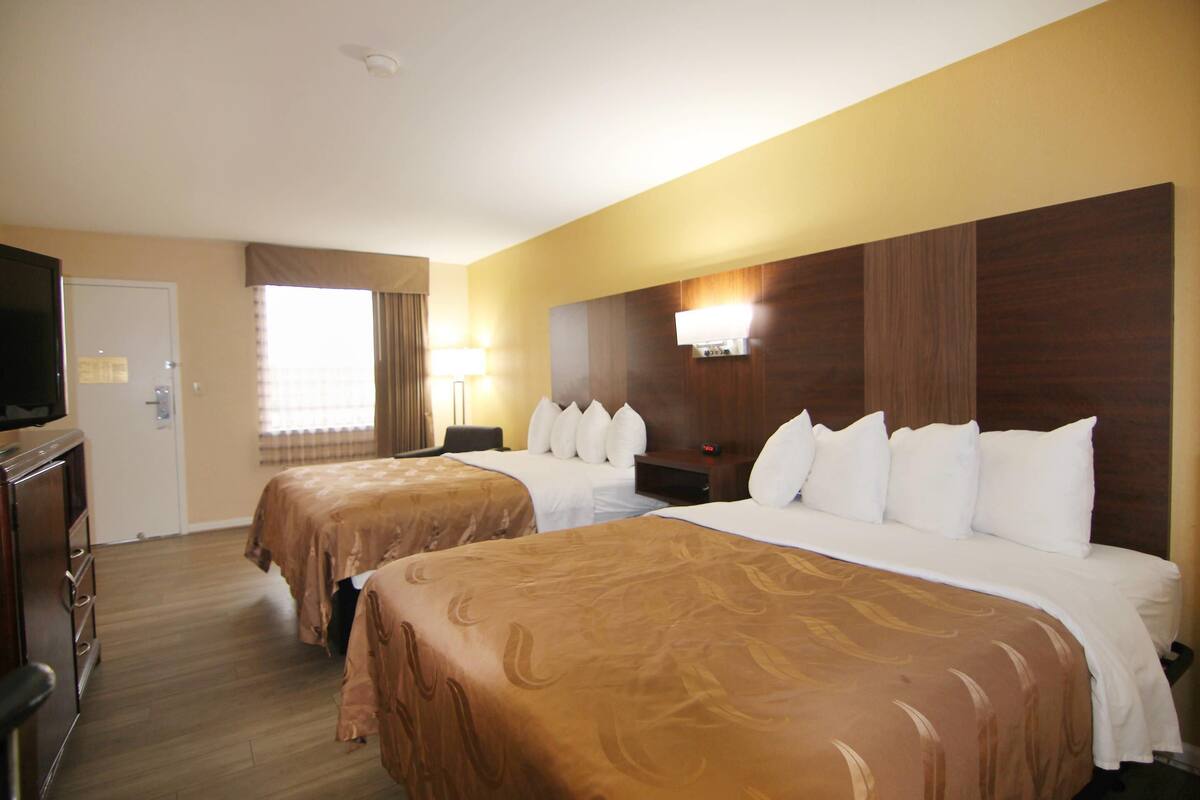 A hotel room with two beds, a television, a desk, and a window with curtains.